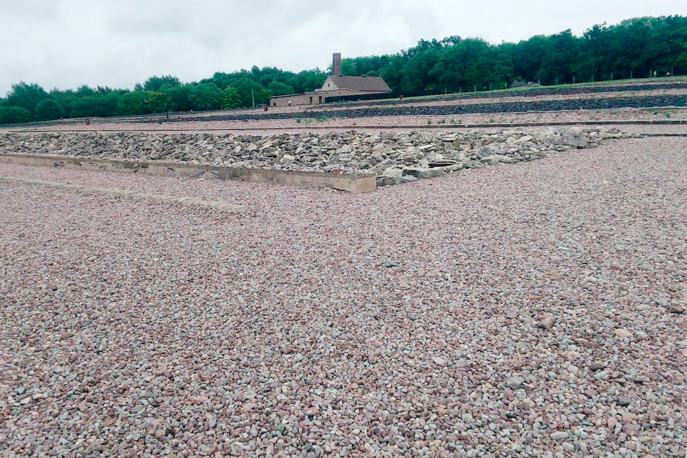 Бухенвальд сейчас выглядит так. Когда его превратили в мемориал, места бараков обозначили камнями. На заднем плане видно здание крематория. По работе я оказывалась в этих местах больше десяти раз, и там всегда была промозглая погода. Жуткое место